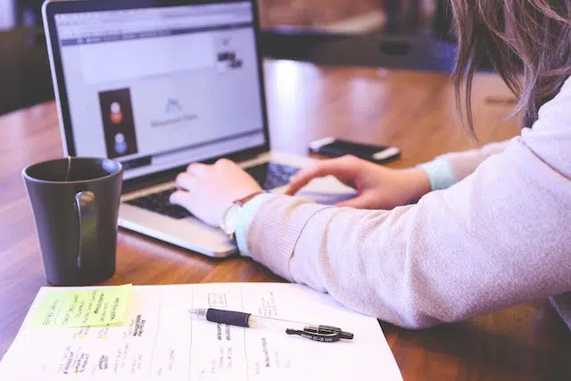 uma pessoa trabalhando com um notebook, com caderno, caneta e xícara na mesa